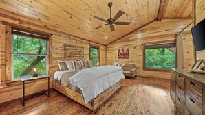 A wooden cabin bedroom with a bed, dresser, and large windows.