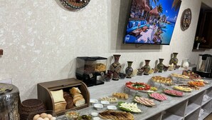 A buffet with various food items and condiments, a television displaying a tropical scene, and decorative vases on the wall. - AKS HOTEL (Tashkent)