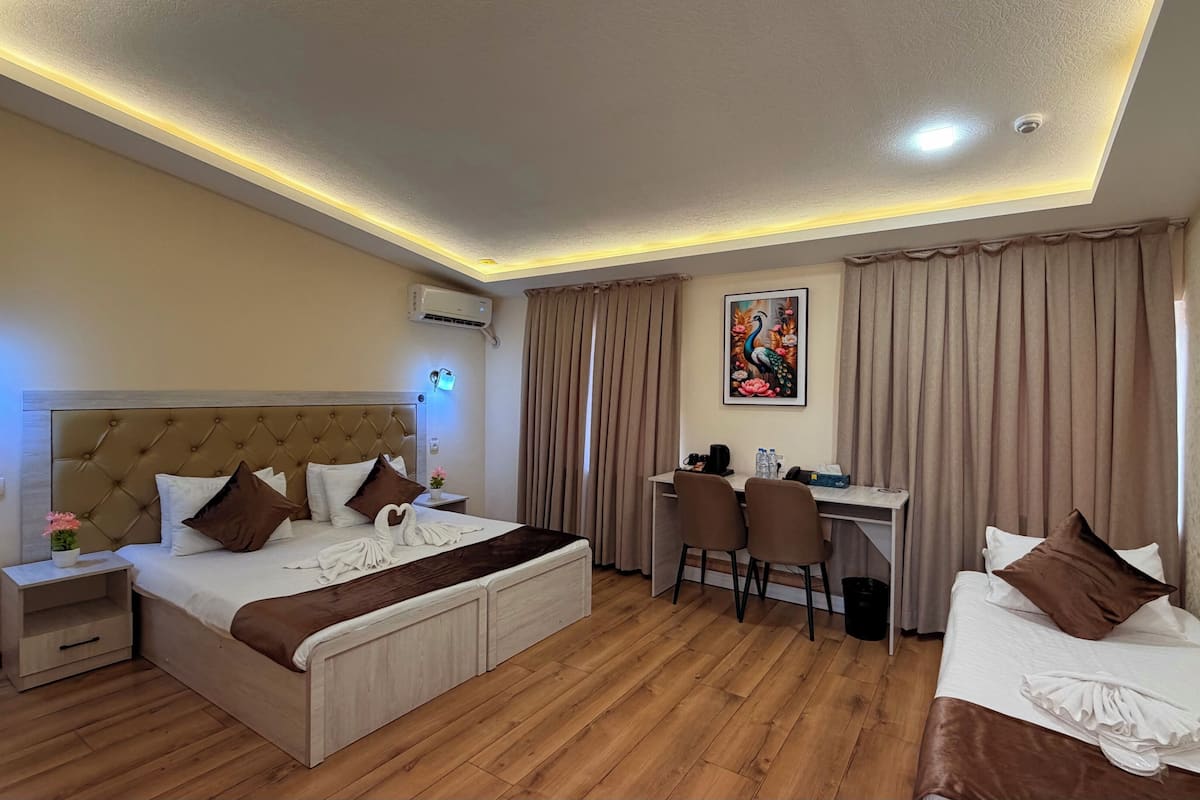 A hotel room with a bed, a desk, two chairs, a painting, and a ceiling light.