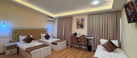 Quarto de hotel com duas camas, uma escrivaninha, cadeiras, um quadro e uma luminária no teto.