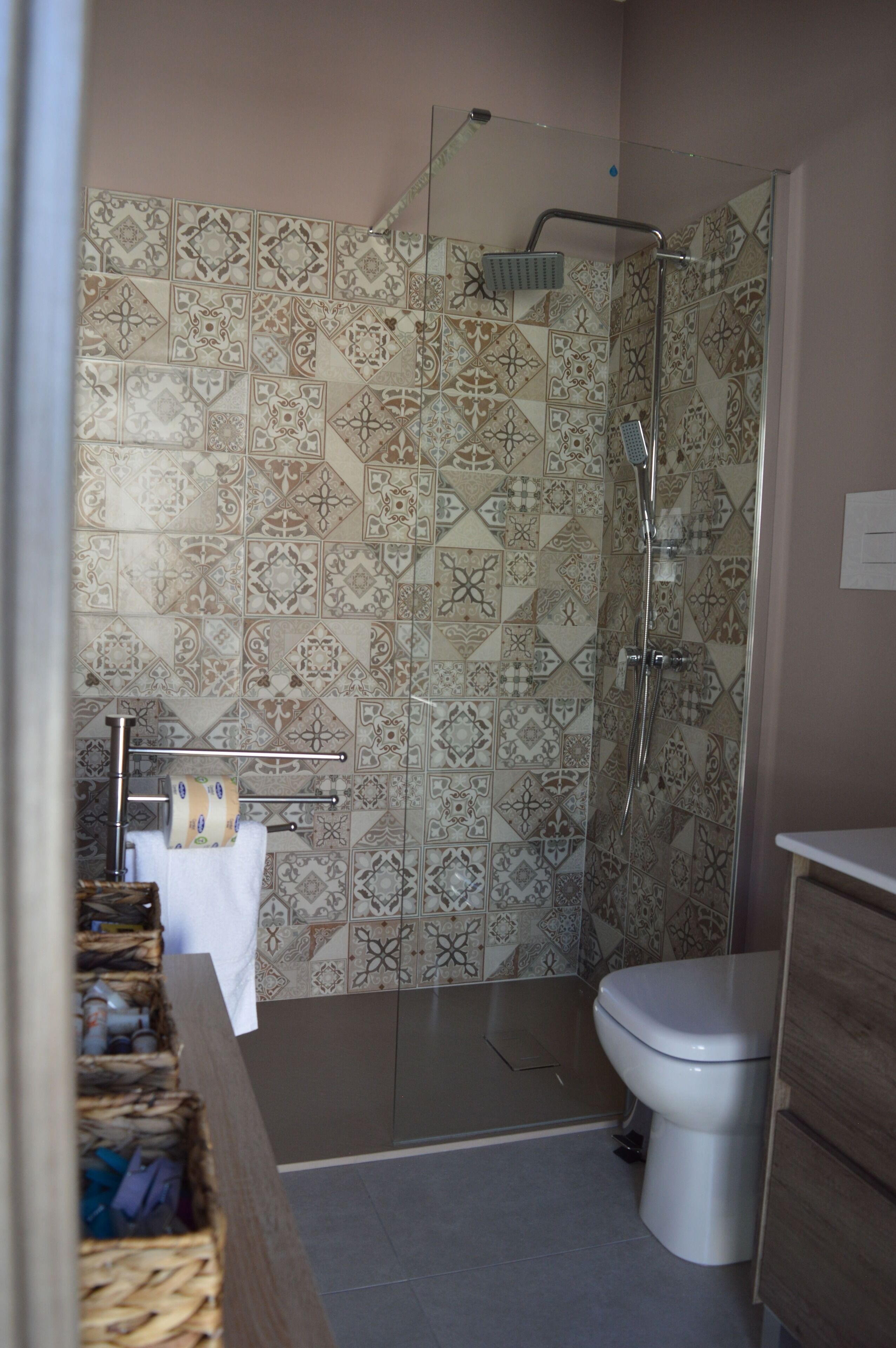 Un baño con baldosas estampadas, cabina de ducha de vidrio, inodoro y tocador de madera con perchero.
