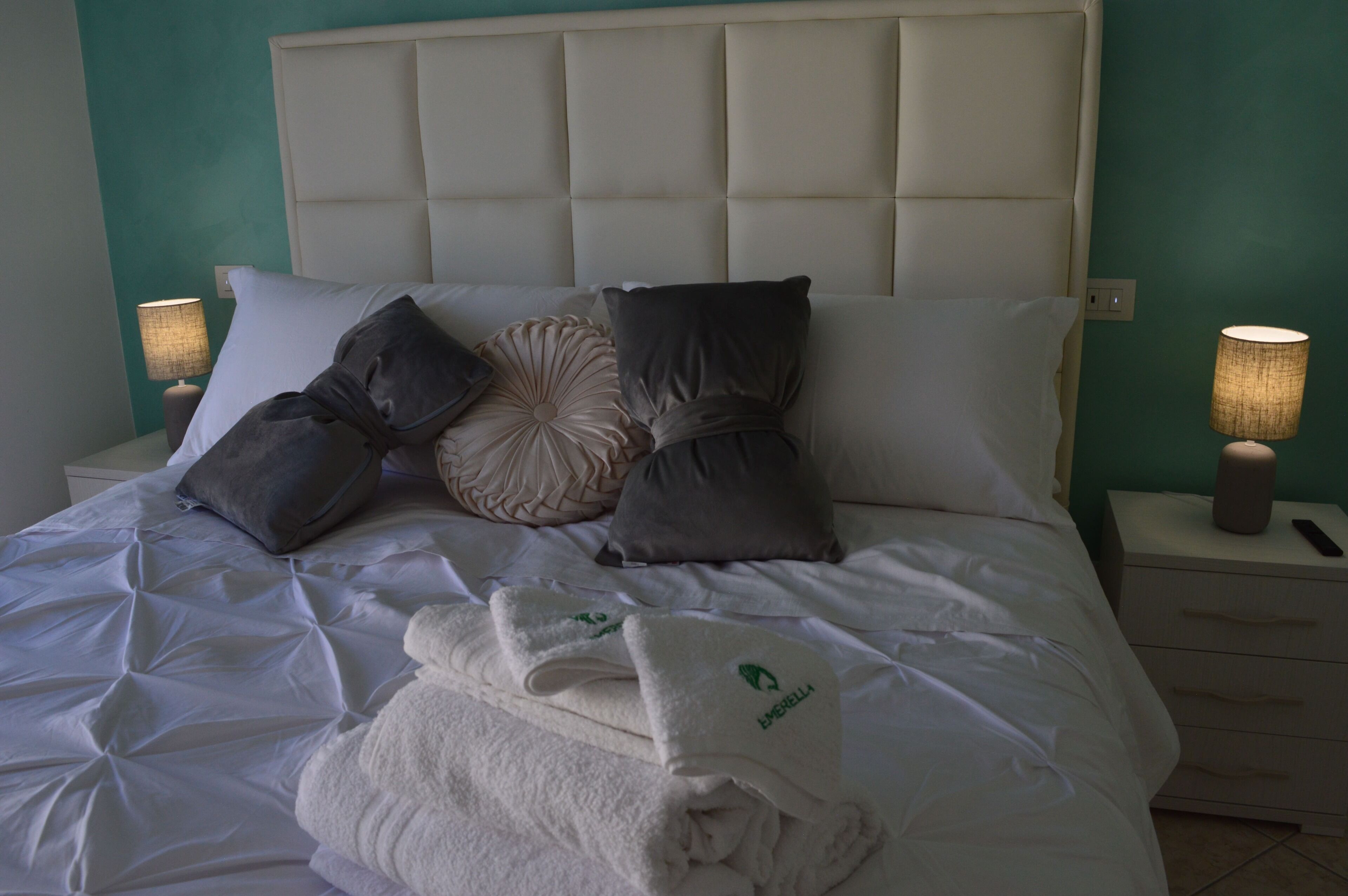 A neatly made bed with a tufted headboard, multiple pillows, and a folded towel on the bed.