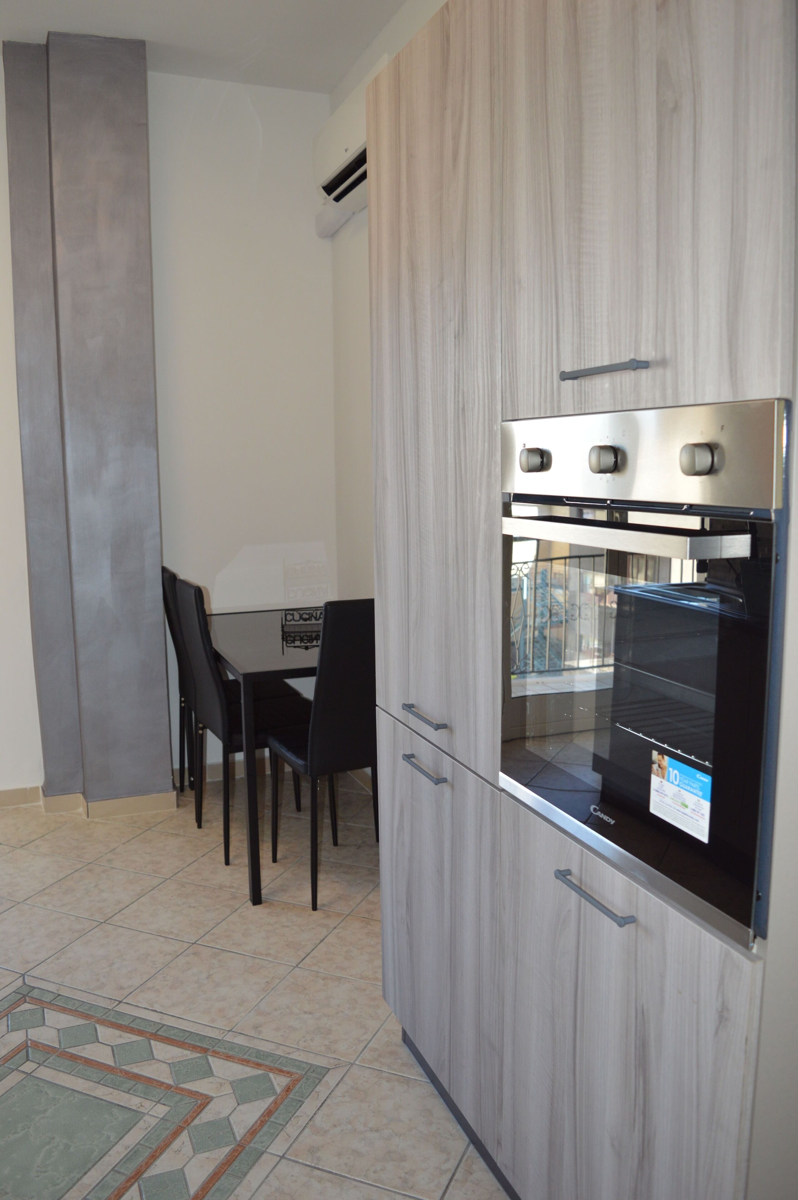 A modern kitchen with a built-in oven, a dining table with chairs, and a tiled floor.