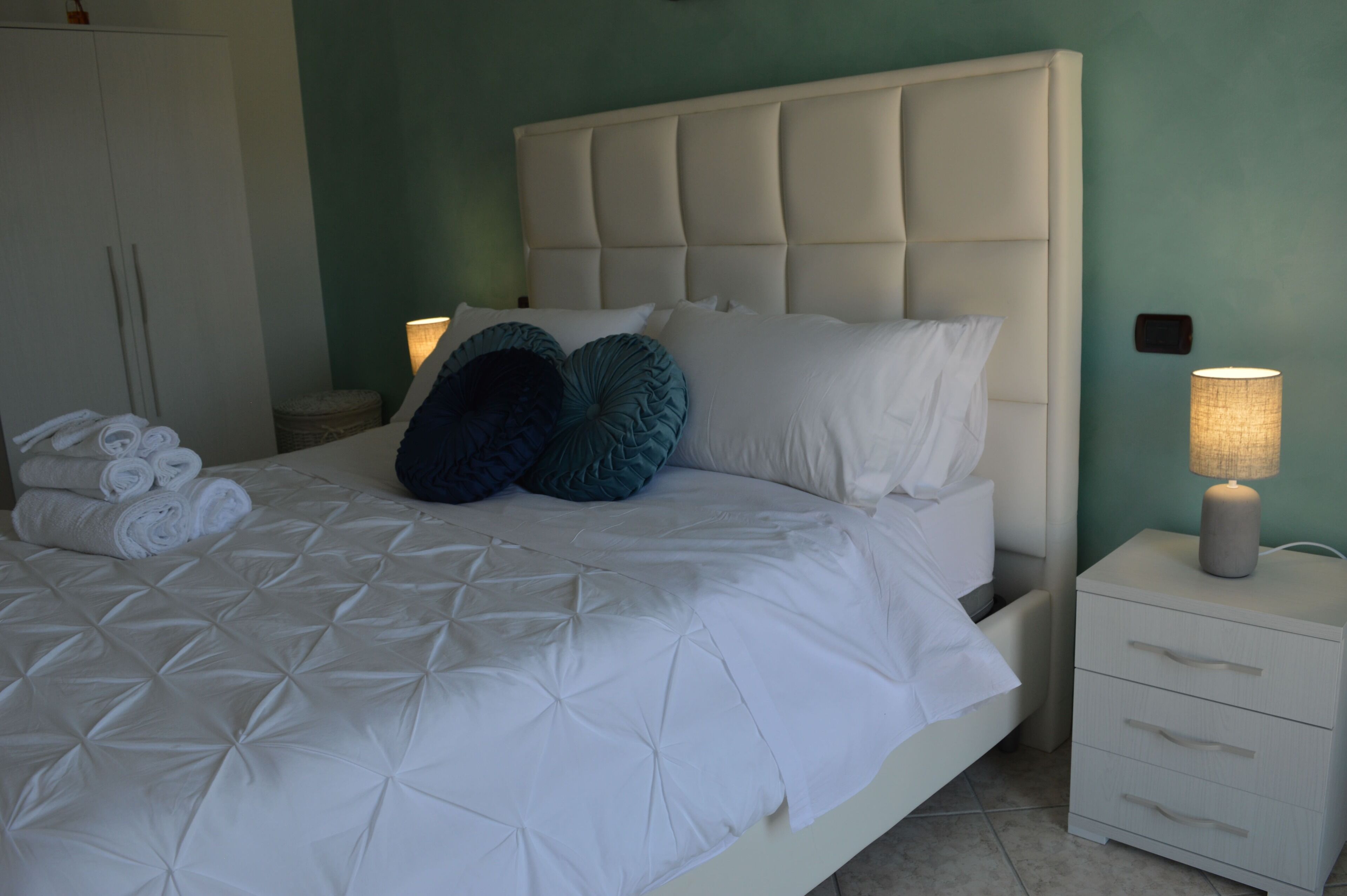 Un lit bien fait, avec une couette blanche matelassée, deux oreillers et des serviettes enroulées posées sur le côté.