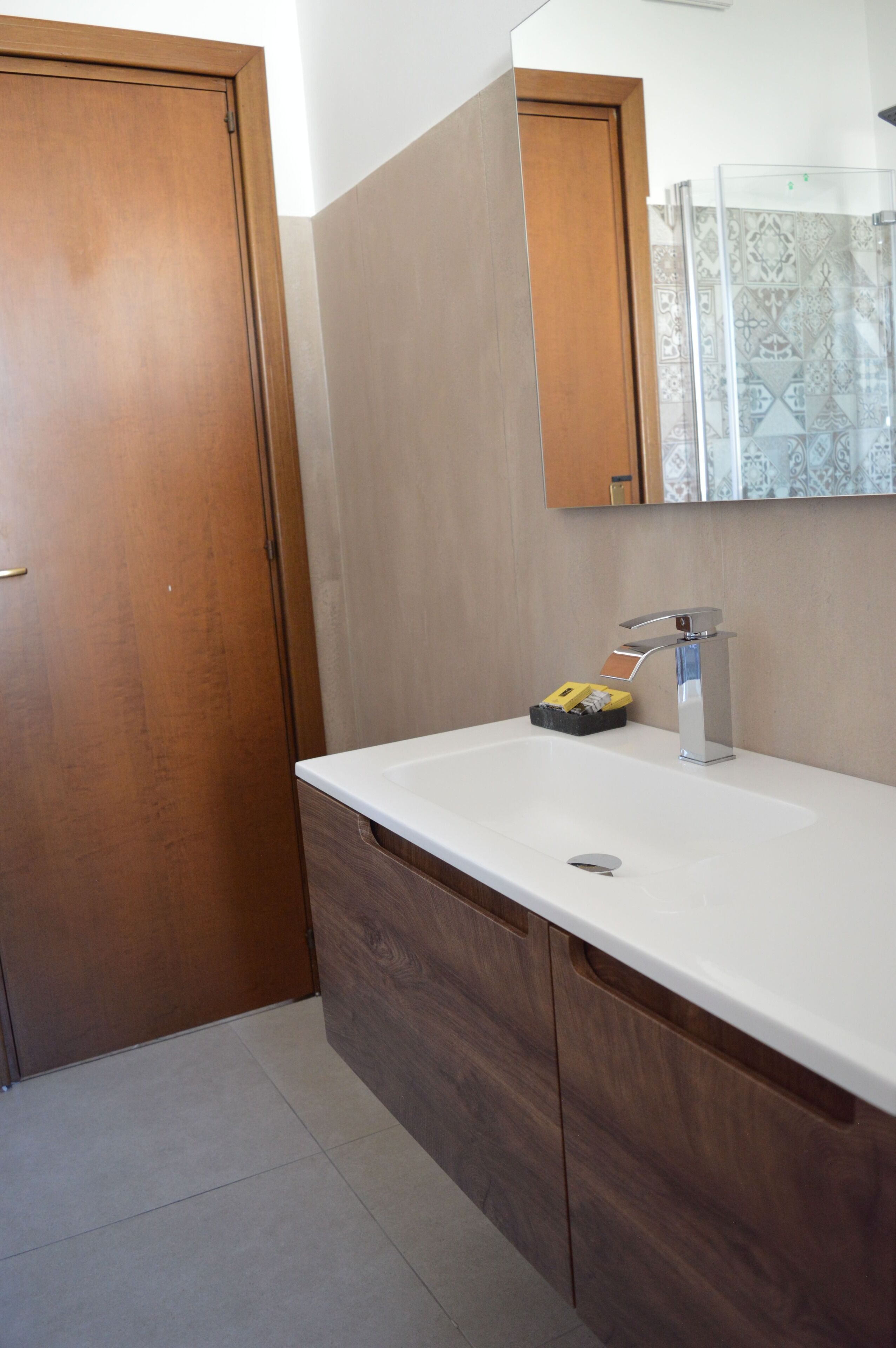 Une salle de bain avec une porte en bois, un lavabo blanc doté d’un robinet moderne, et un miroir au-dessus.