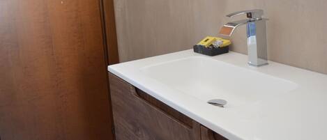 Une salle de bain avec une porte en bois, un lavabo blanc doté d’un robinet moderne, et un miroir au-dessus.
