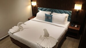 Una cama bien hecha con sábanas blancas y almohadas decorativas con forma de cisne, un cabecero de madera y lámparas de noche.
