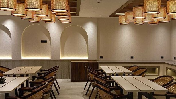 Un restaurante con varias mesas y sillas, diseños de pared en arco y lámparas de mimbre colgantes.