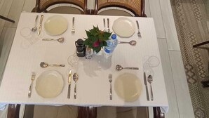 Una mesa de comedor dispuesta con platos, cubiertos y una botella de agua, rodeada de sillas de mimbre.