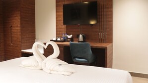 Habitación de hotel con cama, escritorio, televisión y decoración de almohadas con forma de cisne.