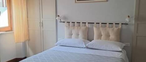 A neatly made bed with a headboard, a window with curtains, and a framed picture on the wall.