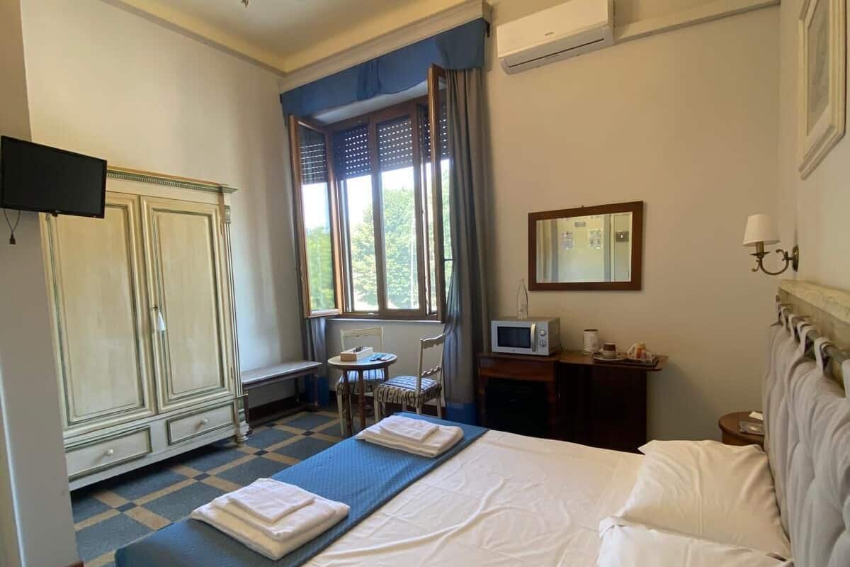 Una habitación de hotel con una cama grande, un escritorio con una computadora, un televisor y un armario.