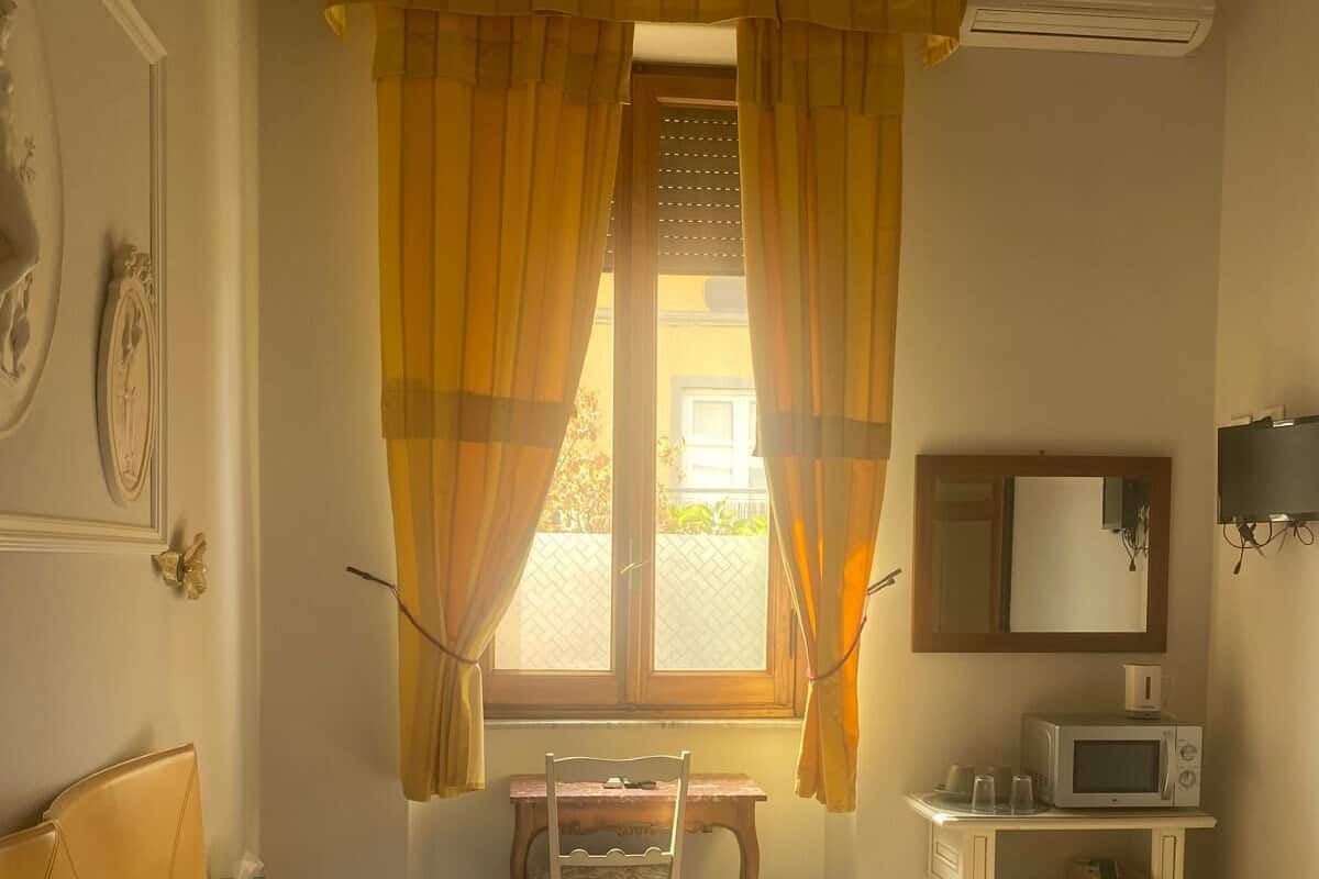 Habitación de hotel con cama, escritorio, silla, microondas y ventana con cortinas.