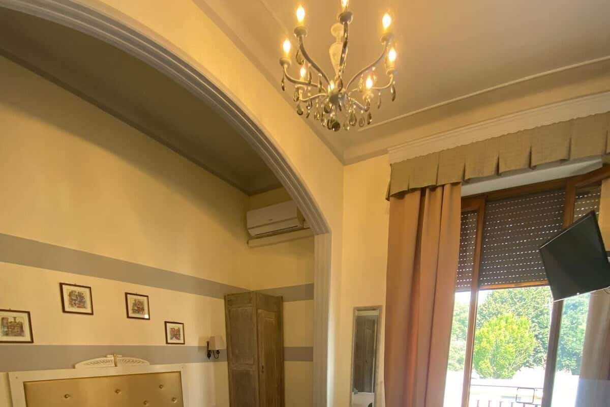 Habitación de hotel con piso a cuadros, una cama con cabecera, un escritorio con una silla, una araña y una ventana con cortinas.