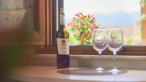 Una bottiglia di vino e due bicchieri su un tavolo vicino a una finestra con vista su fiori e montagne.