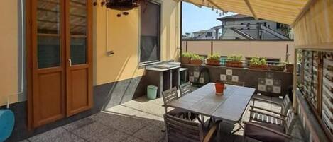 Un patio con mesa y sillas, una planta colgante y una zona cubierta con toldo amarillo.