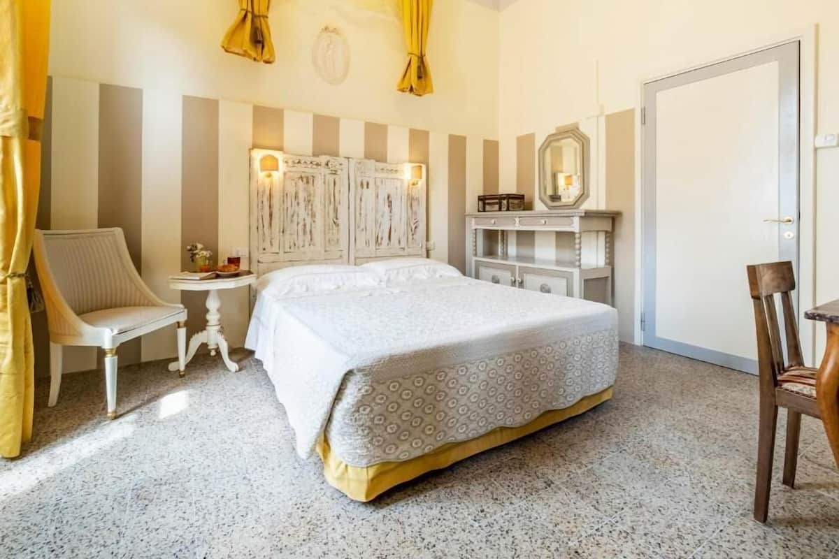Habitación de hotel con una cama grande, una silla, un tocador con espejo y paredes a rayas.