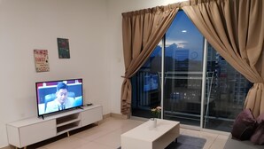 Un salon moderne avec un téléviseur, des meubles blancs, une grande fenêtre avec des rideaux et une vue sur la ville.