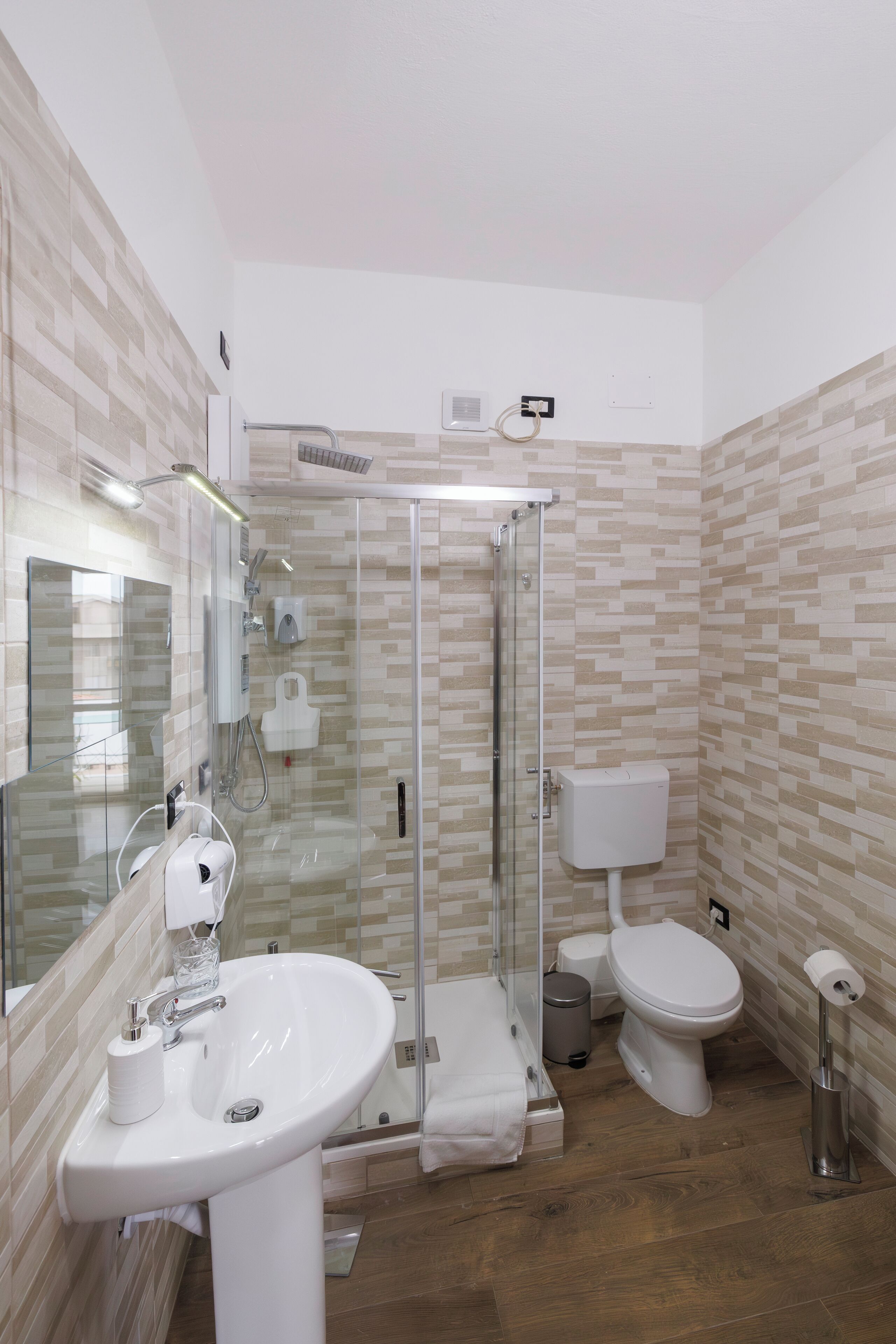 Ein modernes Badezimmer mit einer Duschkabine, einem weißen Waschbecken und einer Toilette.