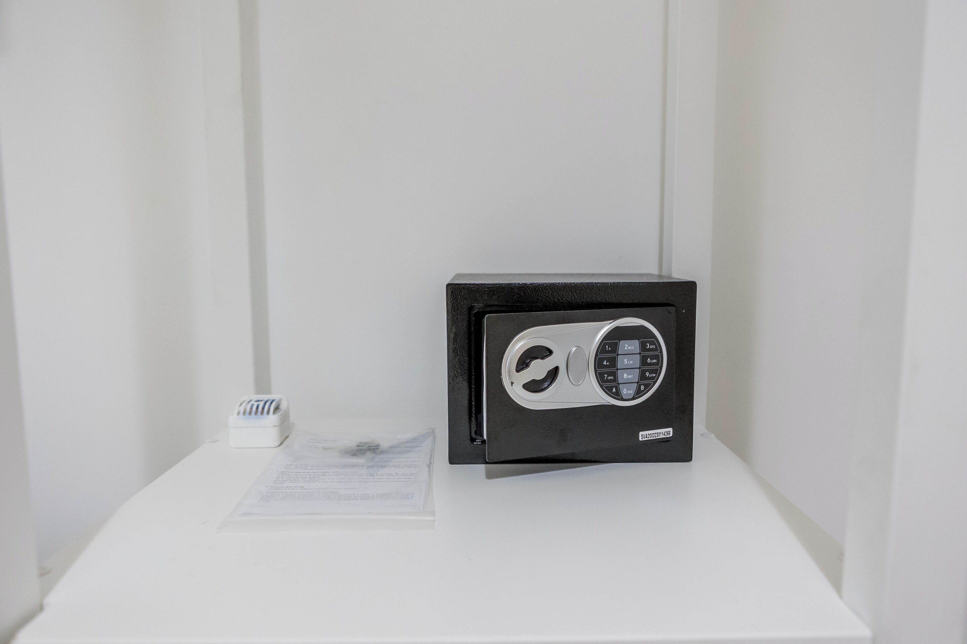A black safe on a white pedestal with a small white object beside it.