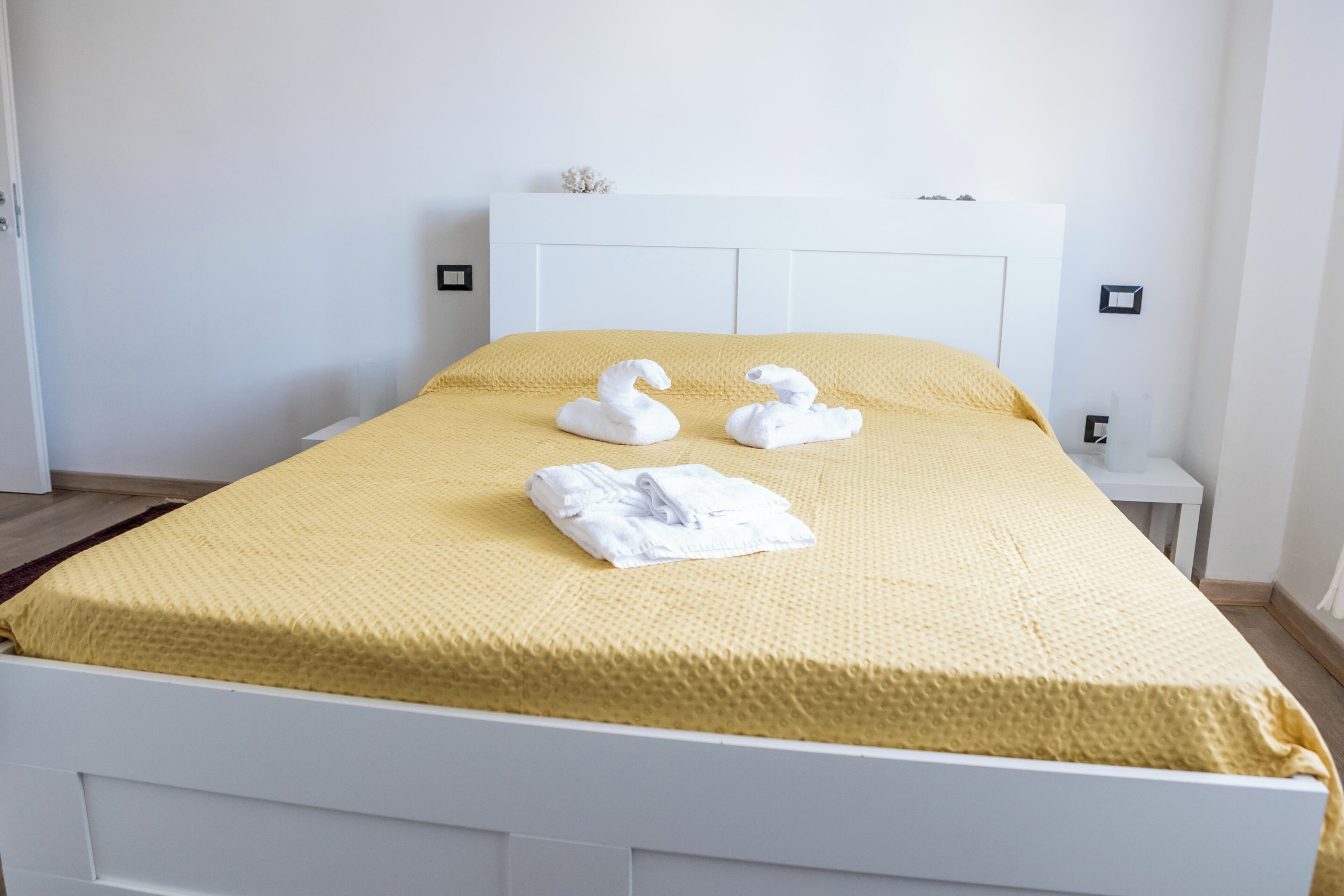 Ein ordentlich bezogenes Bett mit einer gelben Tagesdecke und zwei handtuchförmigen Schwanen.