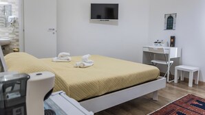 Habitación de hotel con cama, televisión montada en la pared, un pequeño escritorio, una silla y una mesita de noche.