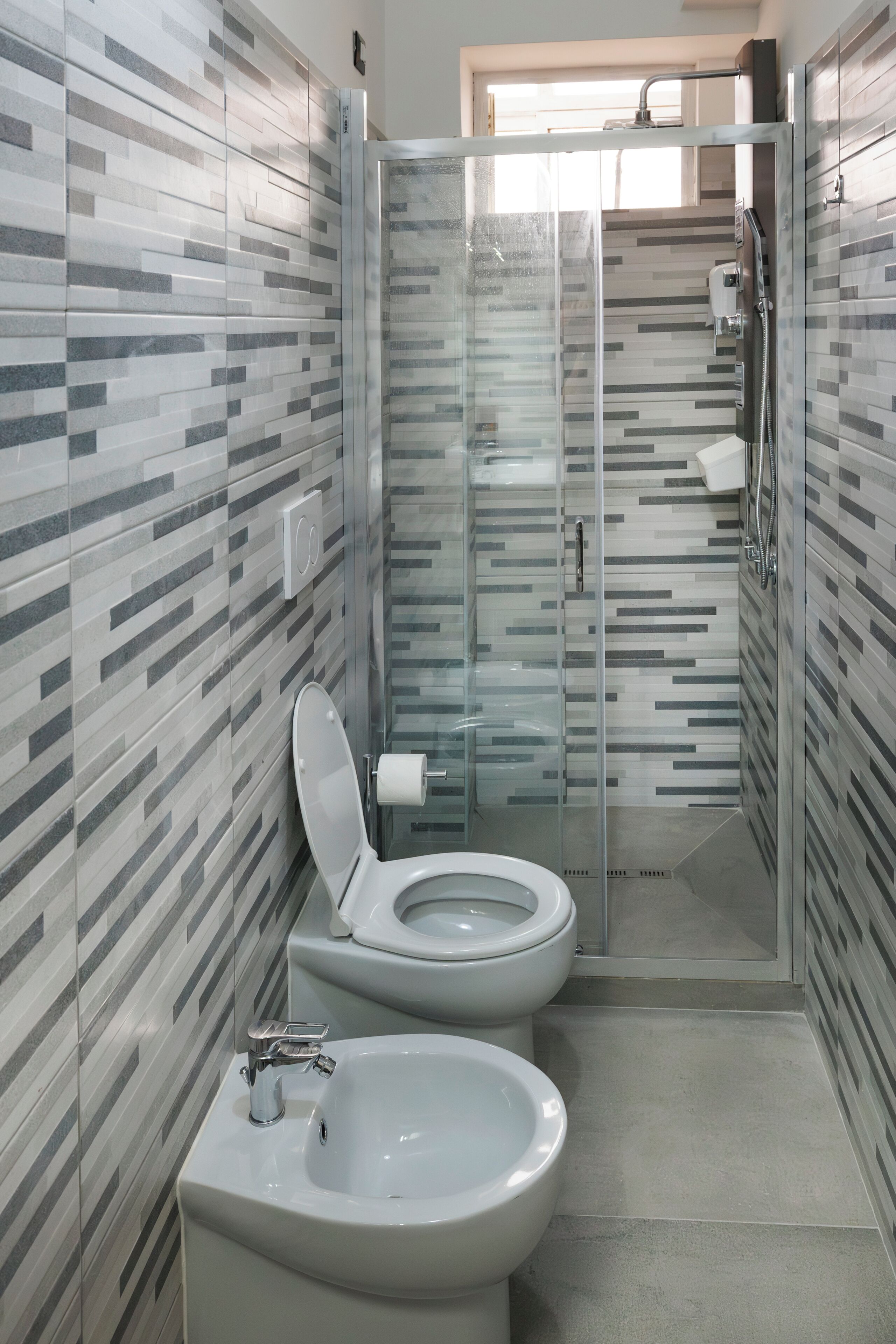 A modern bathroom with a glass-enclosed shower, a toilet, and a bidet.
