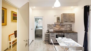 Cocina compacta con comedor, cafetera y vista al cuarto contiguo.