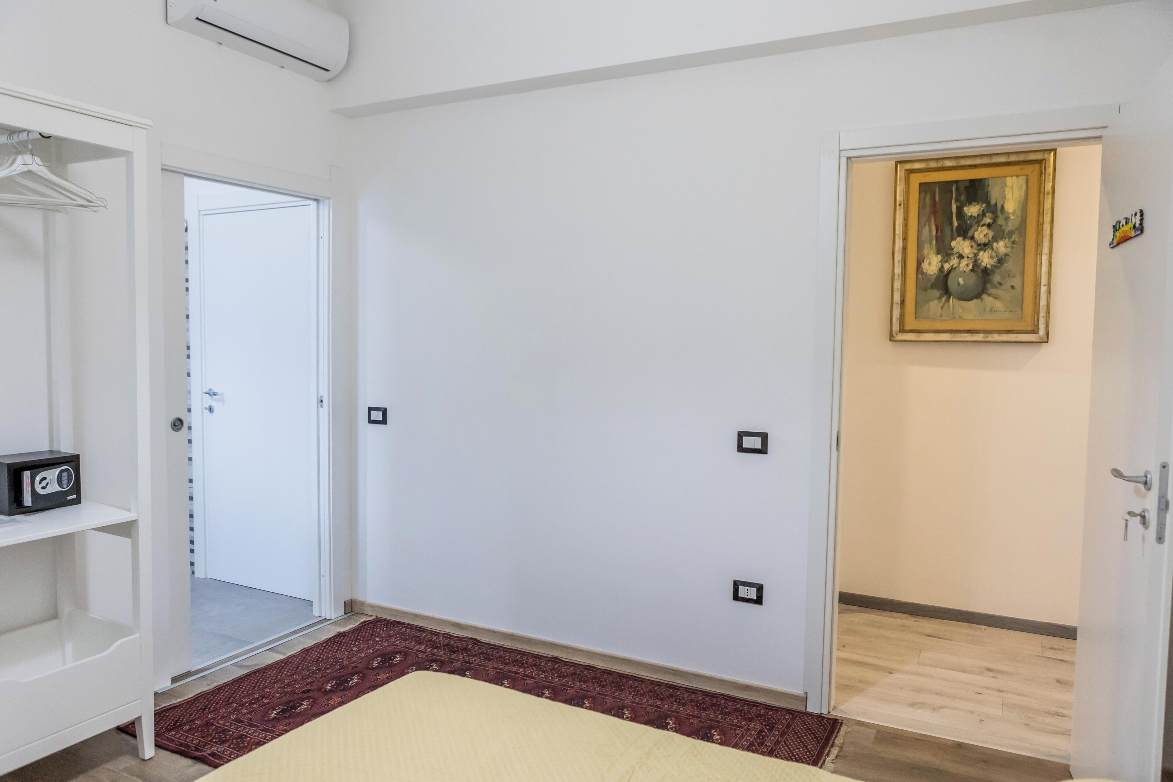 A room with a bed, a wardrobe, a door leading to another room, and a painting on the wall.