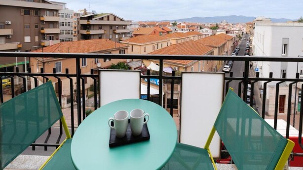 Un balcón con mesa y sillas, con vistas a un paisaje urbano que incluye edificios y una cadena montañosa distante.