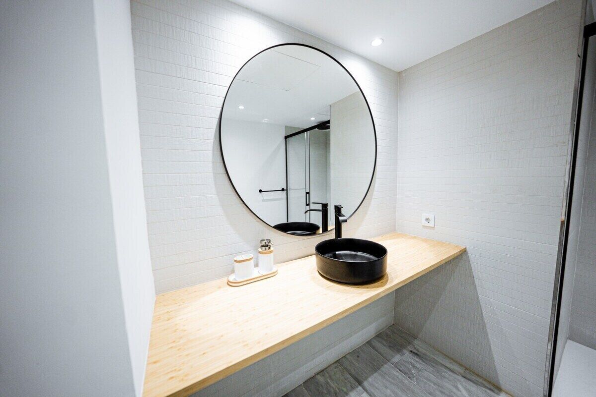 A modern bathroom with a round mirror, a wooden vanity, and a black sink.