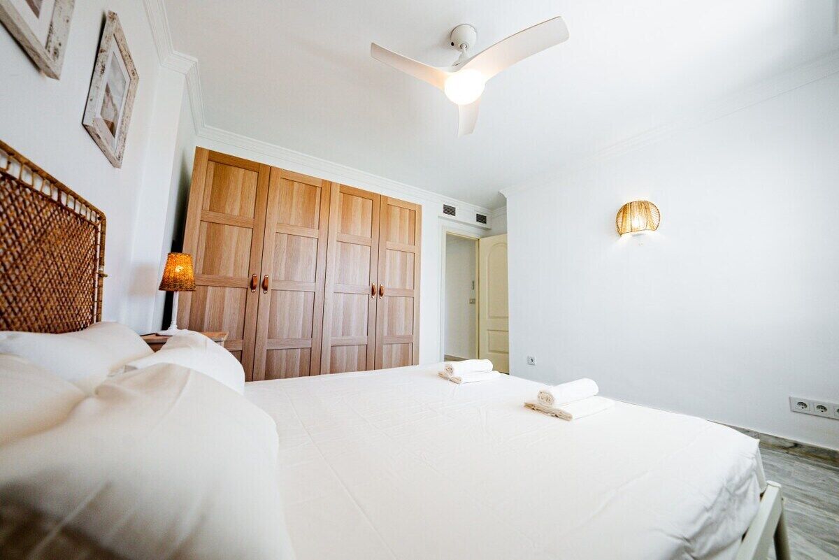 A hotel room with a bed, a wooden wardrobe, a ceiling fan, and a wall-mounted light fixture.