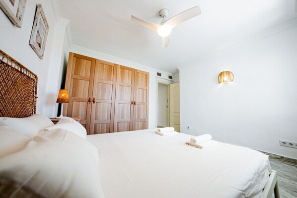 A hotel room with a bed, a wooden wardrobe, a ceiling fan, and a wall-mounted light fixture.