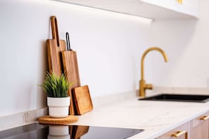 A kitchen with a white countertop, a gold faucet, and wooden utensils.