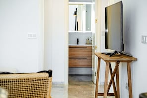 A room with a television on a wooden stand, a wicker chair, a bathroom with a mirror, and a wooden cabinet.