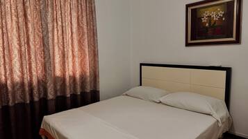 A single bed with a wooden frame and white bedding, a patterned curtain, and a framed artwork on the wall.