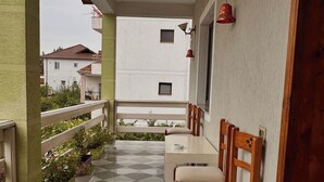 A balcony with a checkered floor, wooden chairs, a table, potted plants, and a view of neighboring buildings. - Grand House  (Tirana)