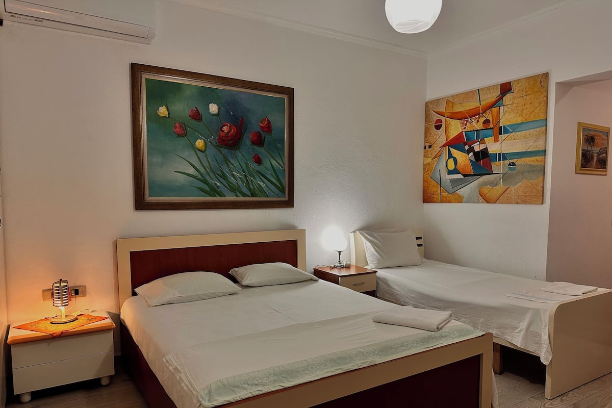 Ein Hotelzimmer mit zwei Betten, einem Nachttisch mit Lampe und zwei Bildern an der Wand.