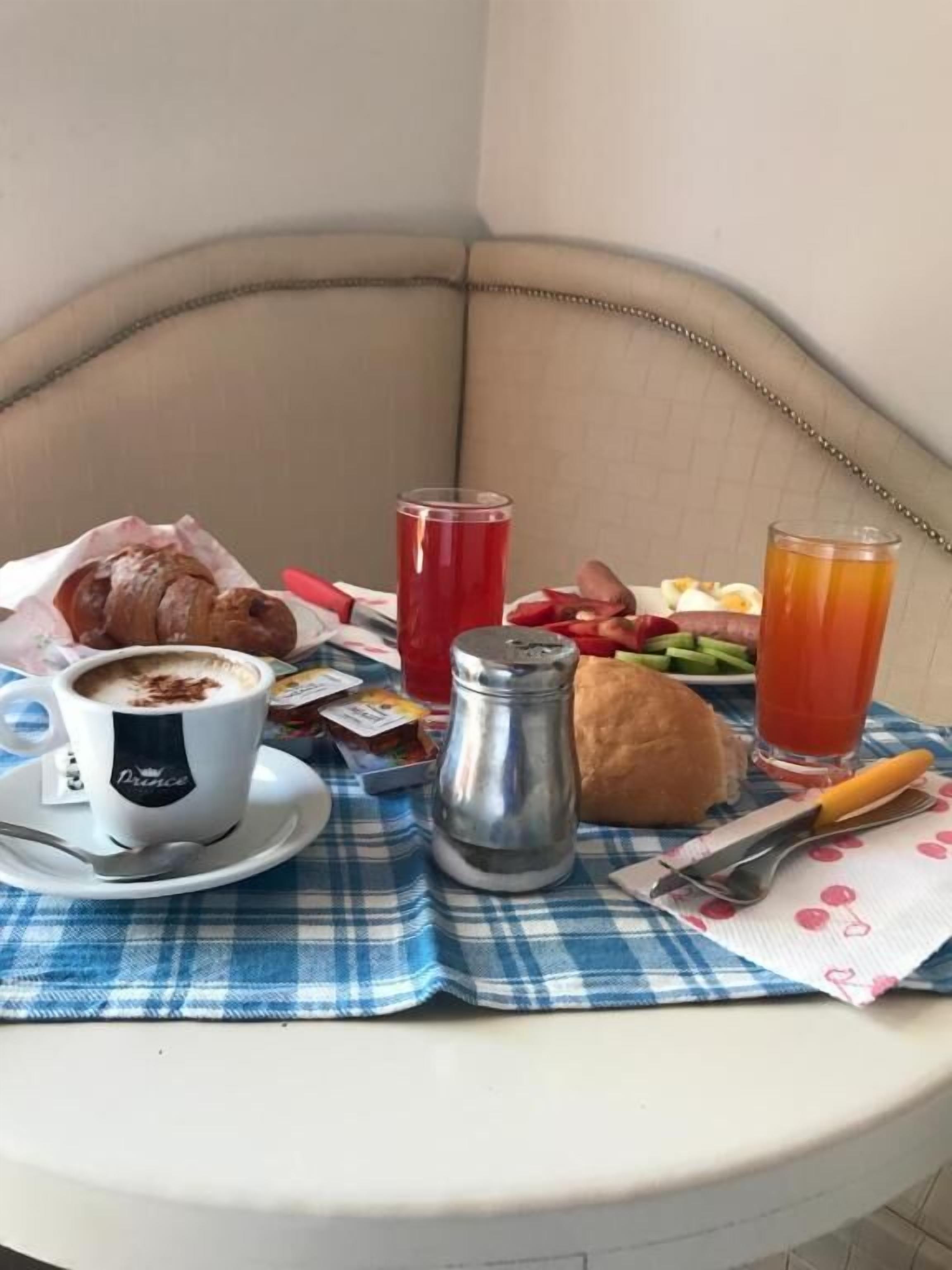 Una mesa redonda con un mantel a cuadros presenta un desayuno que incluye un croissant, café, un salero, un sándwich y dos vasos de jugo.