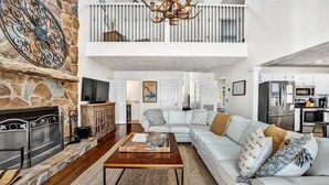 Ein geräumiges Wohnzimmer mit Kamin aus Stein, einer großen Couch, einem Couchtisch und einer Küche im Hintergrund.