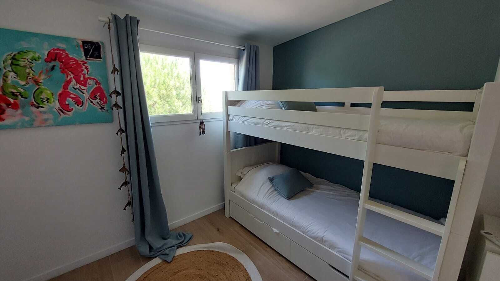 Een kamer met een stapelbed, een raam met gordijnen en een schilderij aan de muur.