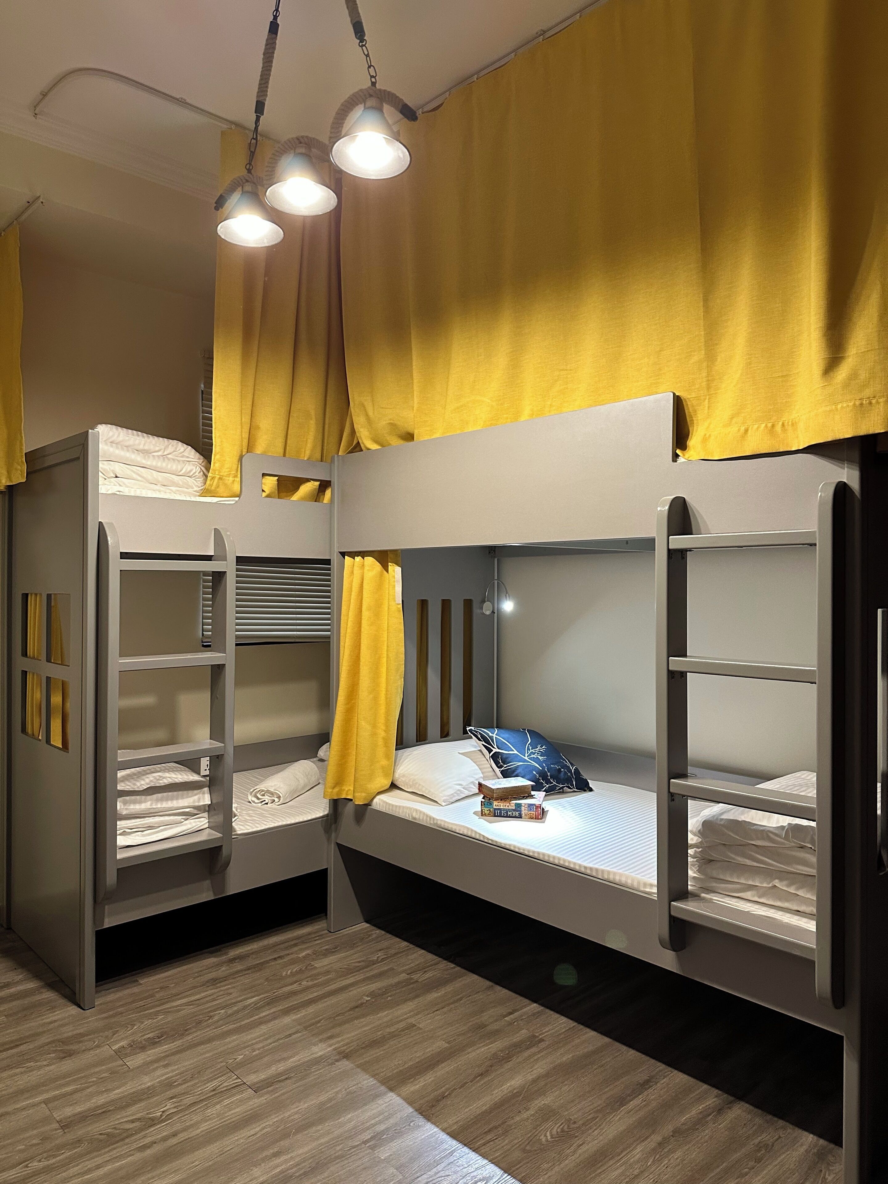 A bunk bed room with a wooden floor, a bed with a blue pillow, and a shelf with books.