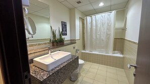 Une salle de bain équipée d’un lavabo, de toilettes et d’une baignoire. Un panneau indiquant les règles d’utilisation des toilettes et une plante ornent le comptoir.