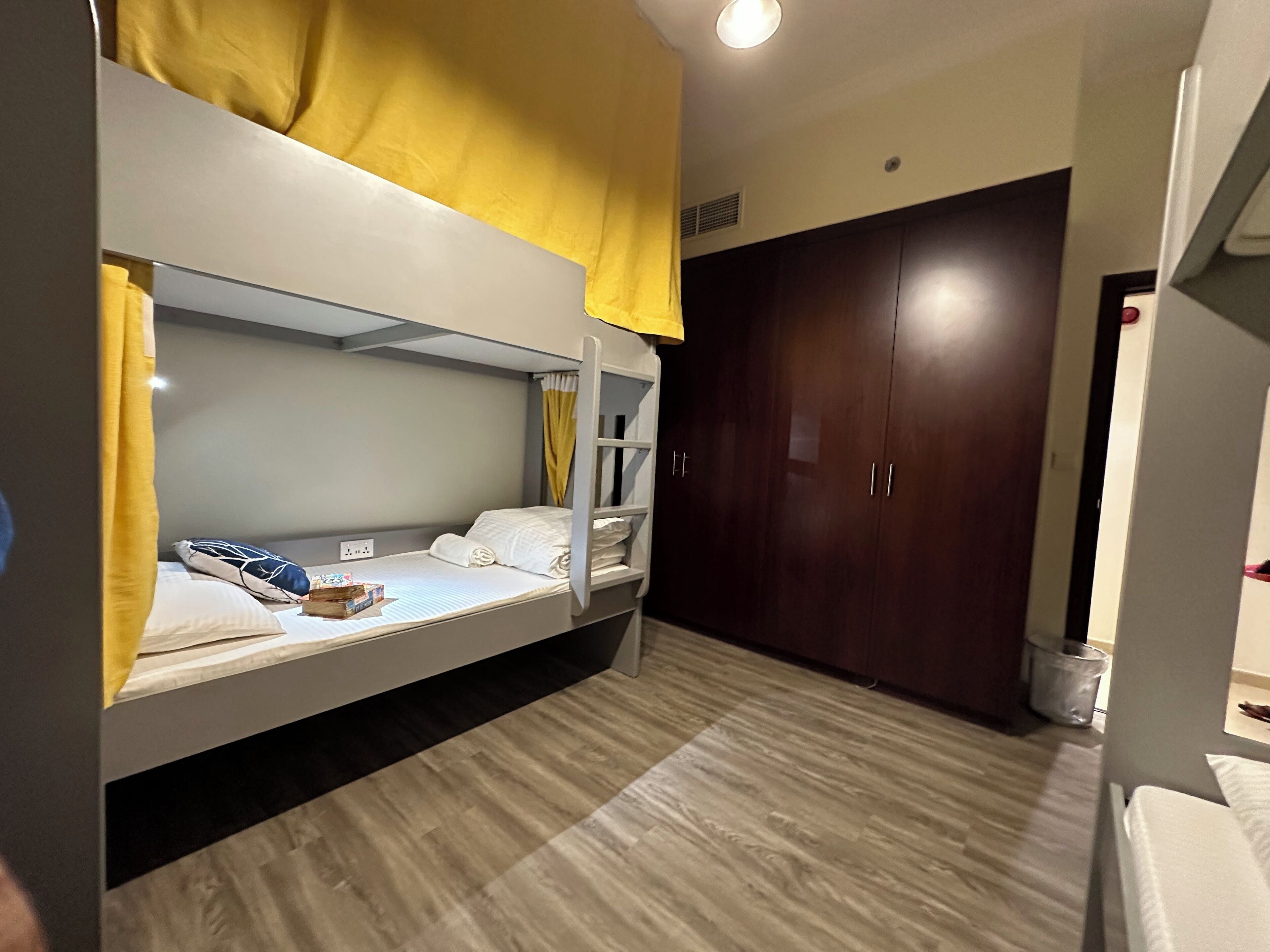 Habitación con literas, suelo de madera, un armario y una cama con cabecera amarilla.
