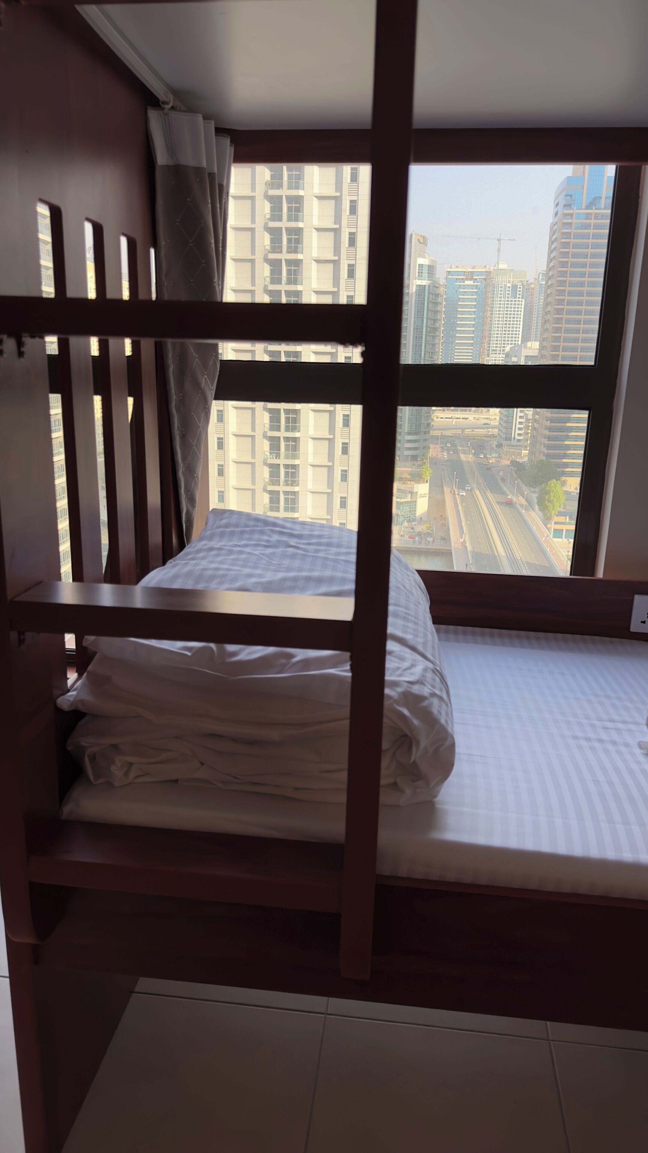Habitación con literas y vista a un paisaje urbano a través de un amplio ventanal.