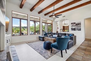 A spacious living room with a large sofa, a blue armchair, and a coffee table. There are large windows offering a view of the outdoors. - Sunrise Retreat- Mtn Views-Pool- Long Term Stays! (Scottsdale)
