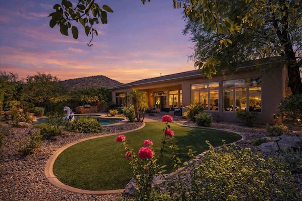 Uma casa moderna com piscina, cercada por um jardim bem cuidado e uma paisagem desértica.