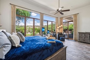 Quarto com uma cama grande, um ventilador de teto, uma mesa com computador e vista para o exterior.