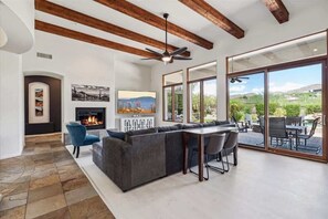 A modern living room with a fireplace, a large sectional sofa, a dining area, and large sliding glass doors leading to an outdoor patio. - Sunrise Retreat- Mtn Views-Pool- Long Term Stays! (Scottsdale)