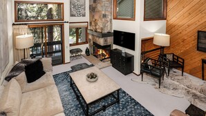 Un salón acogedor con chimenea, asientos cómodos y ventanas amplias que ofrecen vistas al exterior.